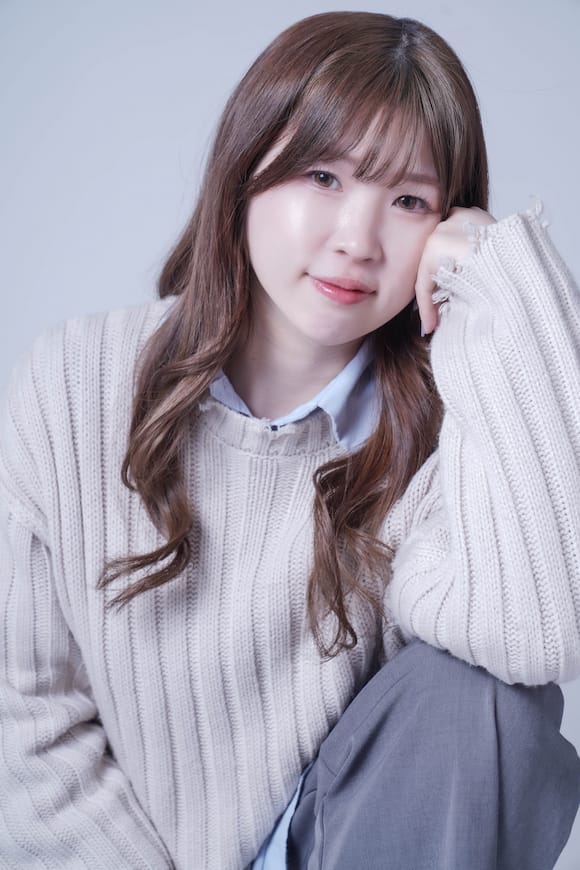 グレー背景でベージュニット×シャツの着座ポートレート、やわらかい雰囲気のプロフィール写真