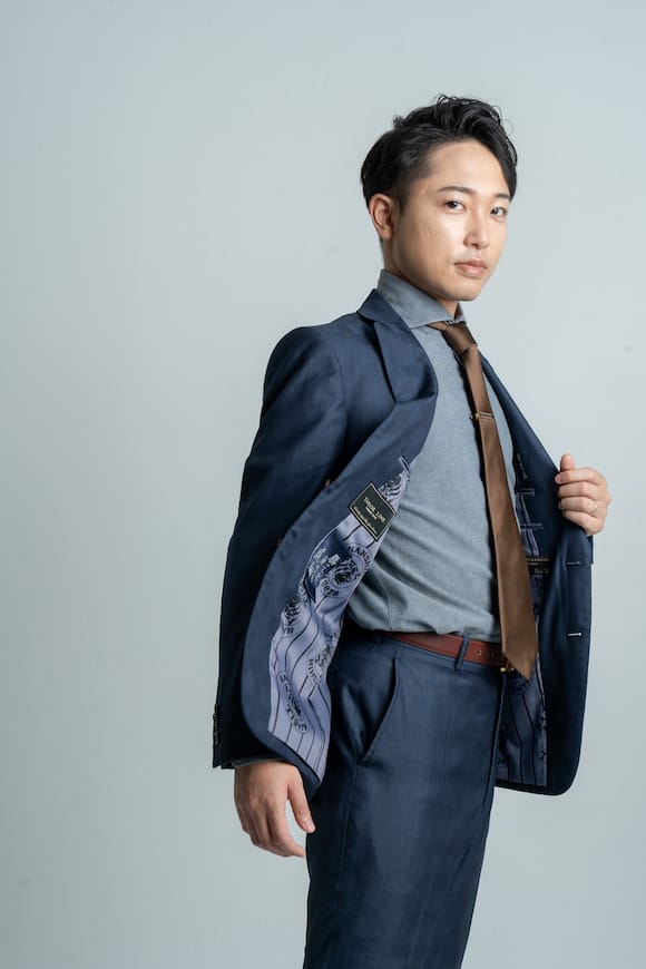 淡いグレー背景でスーツを羽織って見せる立ち姿ポートレート、宣材写真の演出例